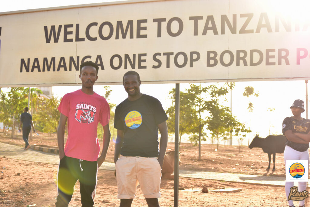 Ngugi Mungai (left) and Arthur Kibugi (right) photographed standing infront of a road welcome sign at theNamanga border.